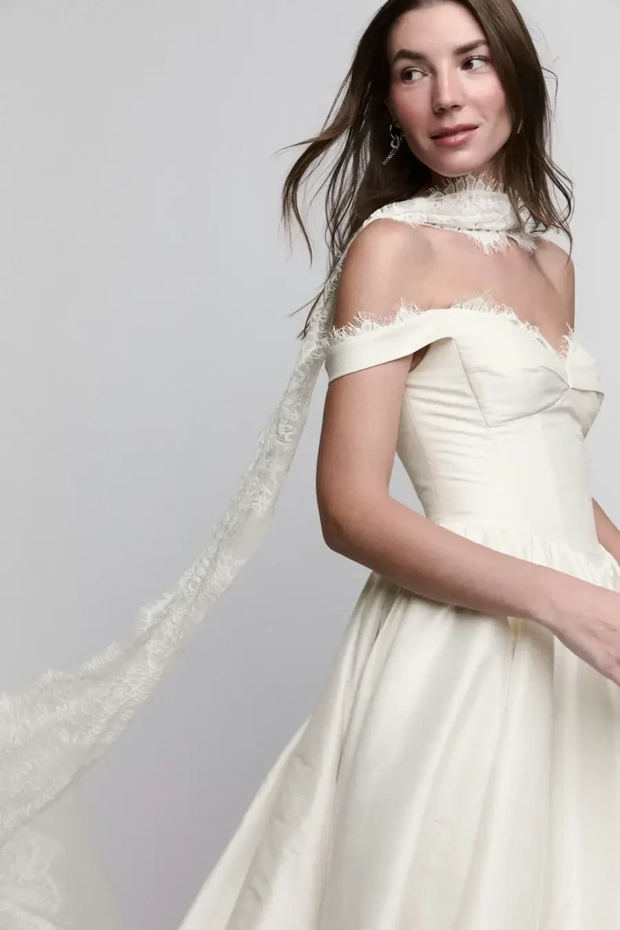 A woman in an elegant off-the-shoulder wedding dress with a flowing lace scarf.